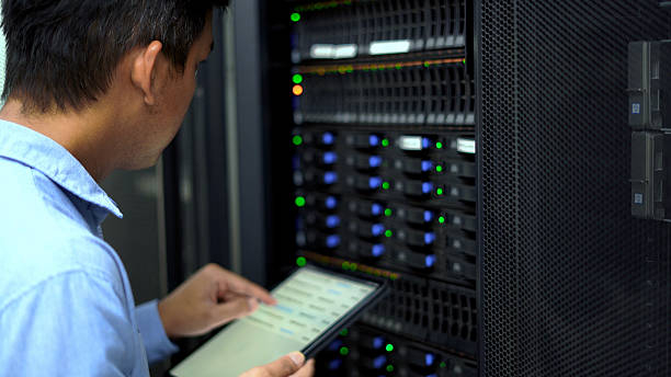 An IT technician inspects and manages a server rack in a data center using a tablet, representing cloud computing, cybersecurity, and network infrastructure maintenance.